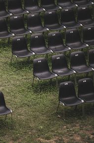 High-angle view of empty black plastic chairs arranged in rows on a grass field.